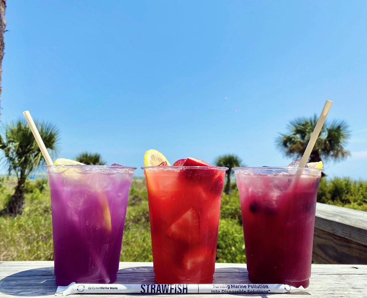 Three cocktail drinks with StrawFish natural Straws fruit against a blue sky and palm trees